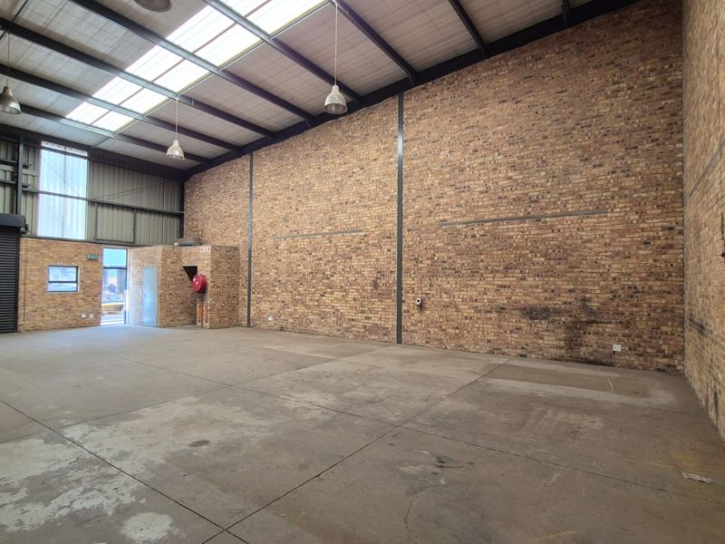 Spacious industrial warehouse unit featuring high ceilings with skylights, exposed brick walls, concrete flooring, and a large roller shutter door for easy access.