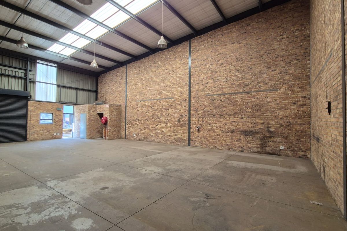 Spacious industrial warehouse unit featuring high ceilings with skylights, exposed brick walls, concrete flooring, and a large roller shutter door for easy access.