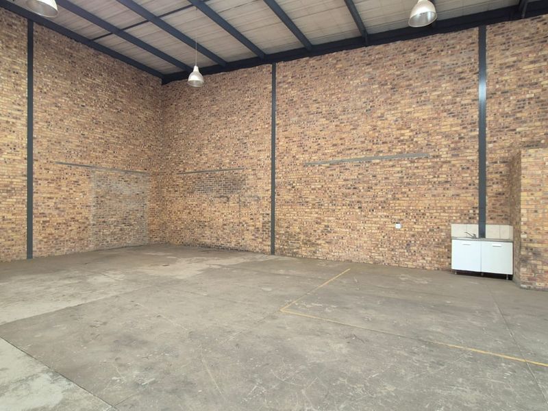 Spacious industrial utility area featuring exposed brick walls, high ceilings with steel portal framing, concrete flooring, and a small built-in kitchenette unit.