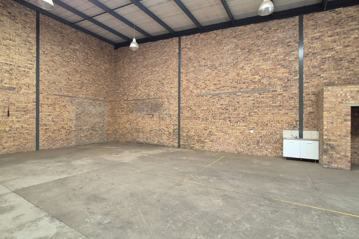 Spacious industrial utility area featuring exposed brick walls, high ceilings with steel portal framing, concrete flooring, and a small built-in kitchenette unit.