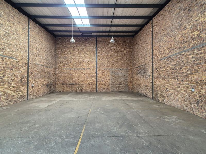Spacious industrial utility area featuring exposed brick walls, high steel truss ceilings with a skylight, and durable concrete flooring.