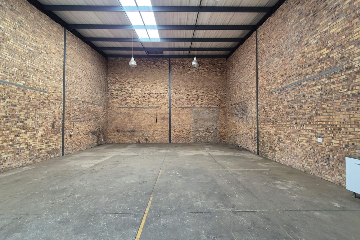 Spacious industrial utility area featuring exposed brick walls, high steel truss ceilings with a skylight, and durable concrete flooring.