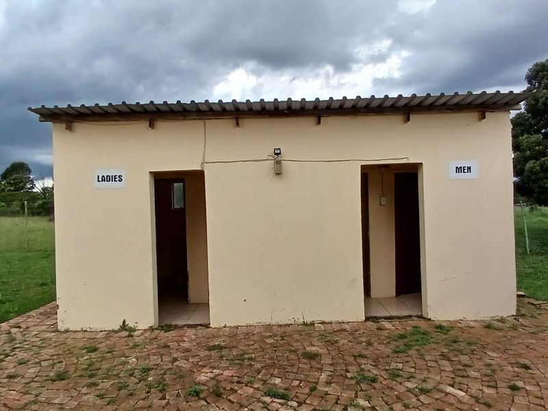 A detached utility building featuring separate male and female restroom entrances, finished with a corrugated metal roof and a brick paved exterior area.