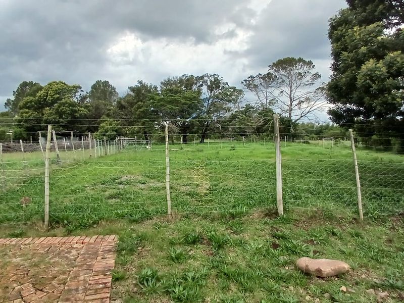 A view of a grassy farm garden area enclosed by wire fencing with wooden posts and a section of brick paving in the foreground.