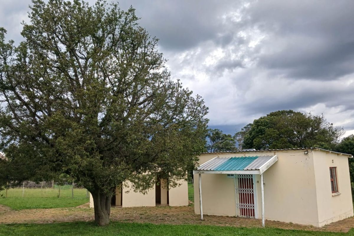 A view of the farm outbuildings featuring simple masonry construction, corrugated roofing, and security gates set within a grassy landscape.