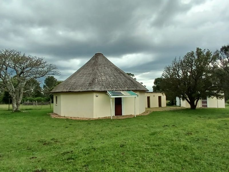 A traditional round farmhouse with a thatched roof, featuring a small solar-powered entrance canopy set within a spacious rural garden.