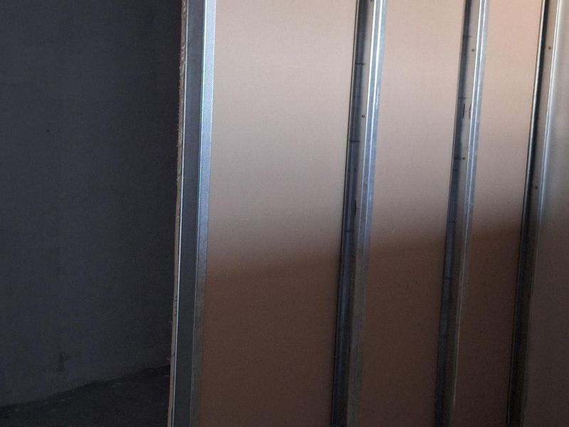An interior space under construction featuring exposed metal stud framing and partially installed gypsum board wall panels.