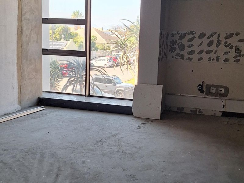 An unfinished open-plan commercial space featuring an exposed ceiling grid, concrete flooring, and large windows providing natural light and street views.