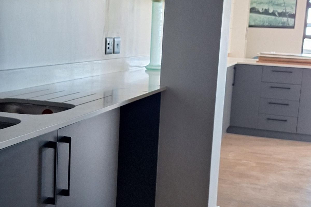 Modern kitchen area featuring dark cabinetry, stone countertops, and wood-look laminate flooring in an open-plan layout.