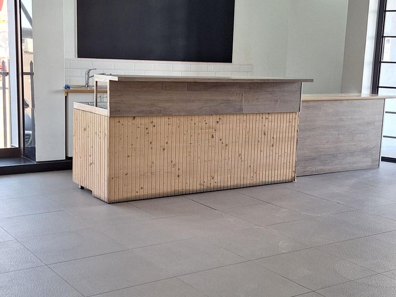 A bright, open-plan commercial space featuring neutral tiled flooring, recessed lighting, and a built-in service counter with a clean, modern aesthetic.