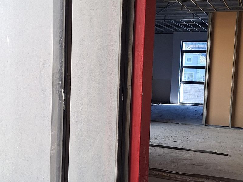 An unfinished commercial open-plan space featuring exposed ceiling grids, concrete flooring, and large sliding glass doors leading to an exterior area.