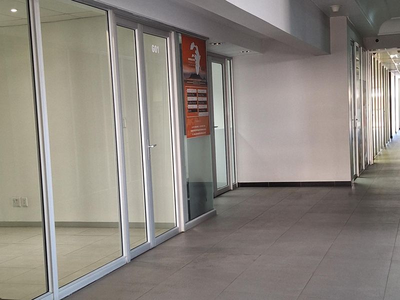 A clean, modern commercial hallway featuring tiled flooring, recessed lighting, and glass-partitioned office spaces.