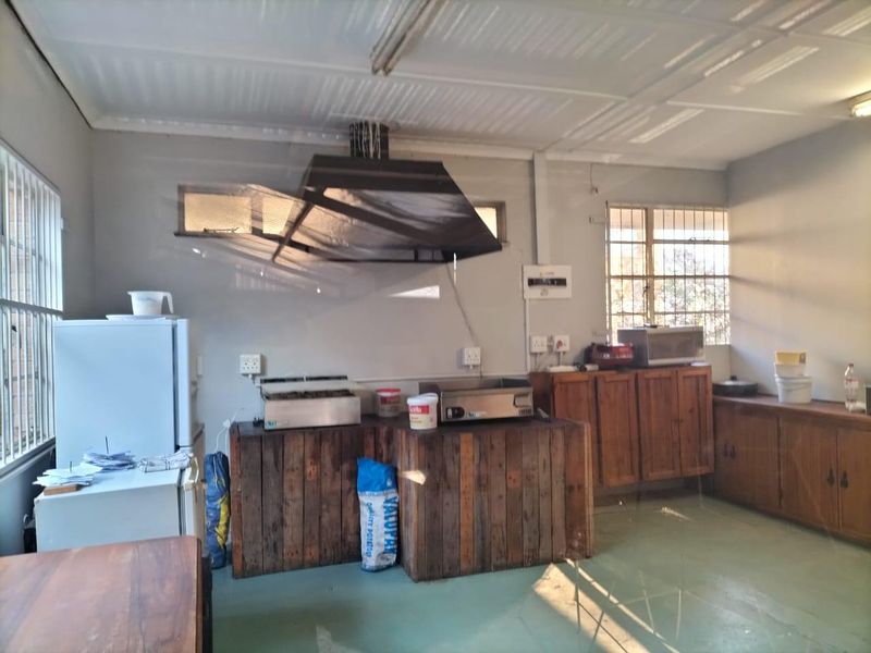 Commercial kitchen area featuring built-in wooden cabinetry, an extractor fan, and security bars on windows, suitable for food preparation or utility use.