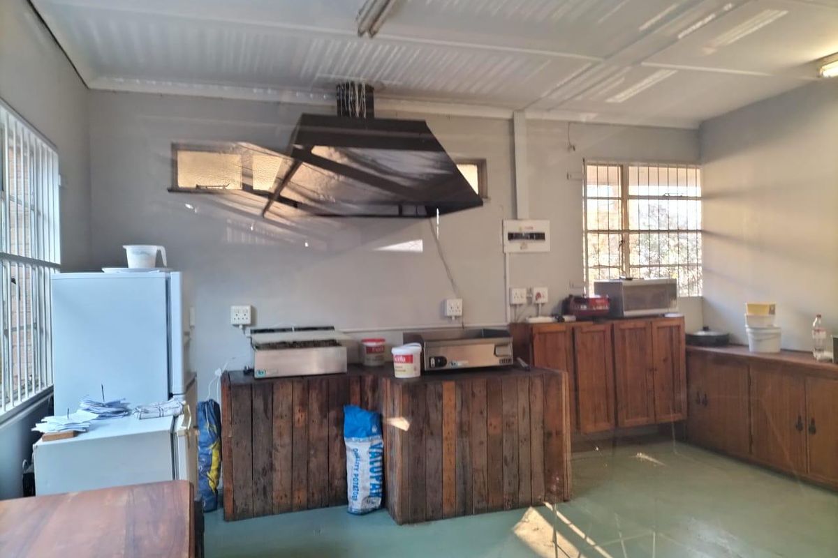 Commercial kitchen area featuring built-in wooden cabinetry, an extractor fan, and security bars on windows, suitable for food preparation or utility use.