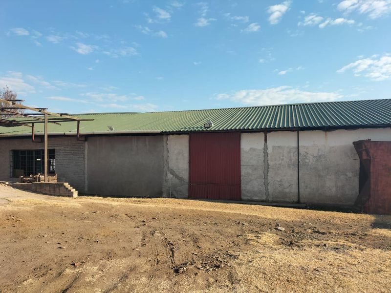 Rear view of a commercial warehouse building featuring a corrugated metal roof, large sliding metal door, and weathered exterior wall finishes.