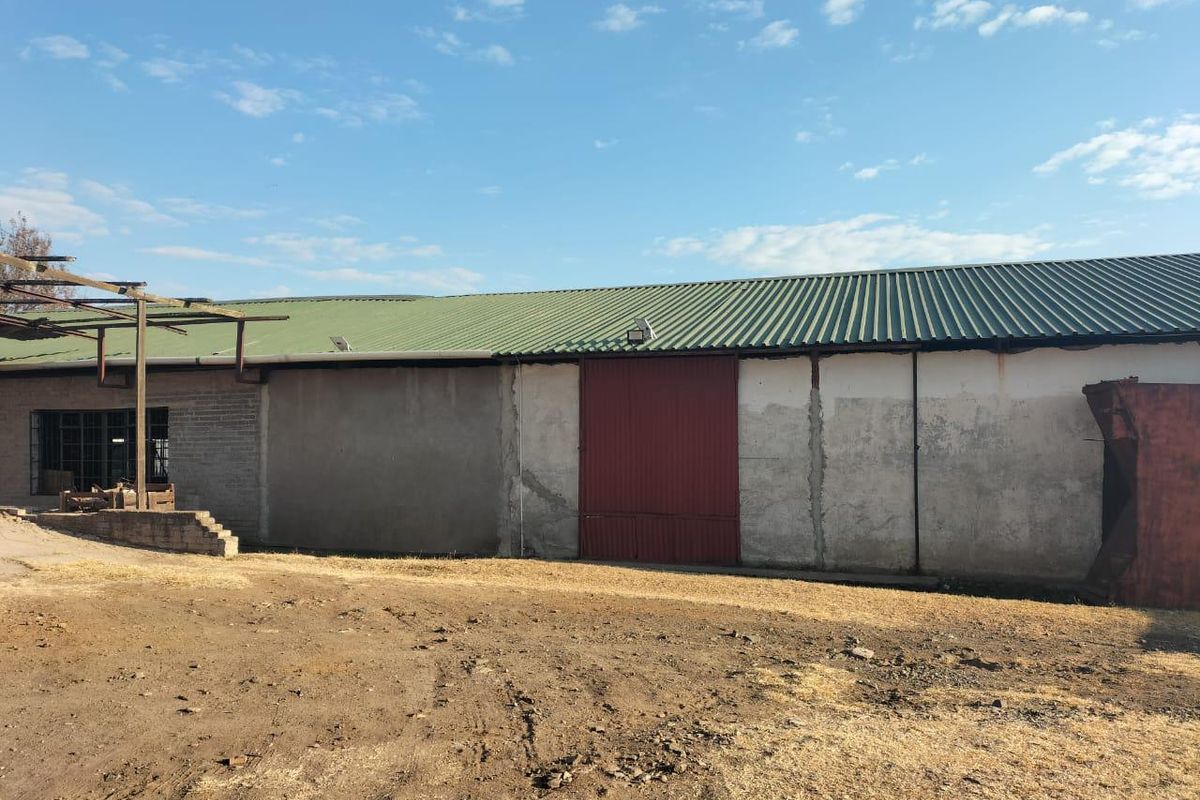 Rear view of a commercial warehouse building featuring a corrugated metal roof, large sliding metal door, and weathered exterior wall finishes.