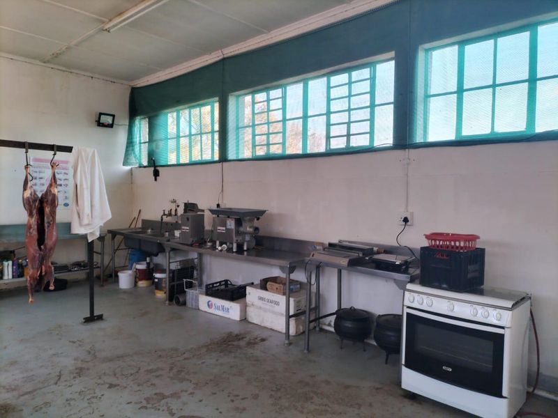 Commercial utility and meat processing area featuring stainless steel work surfaces, industrial equipment, a commercial sink, and a freestanding oven.