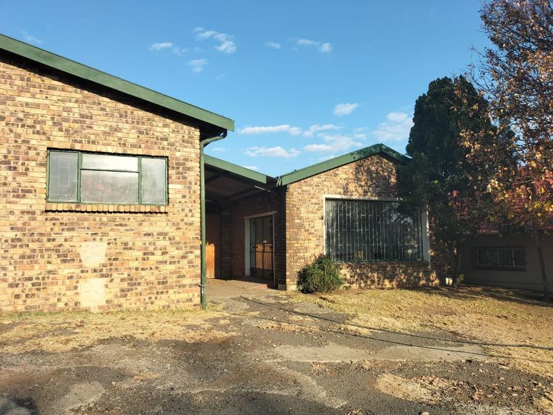 Front exterior view of a face-brick commercial building featuring a covered entrance, security bars on windows, and an asphalt driveway in need of maintenance.