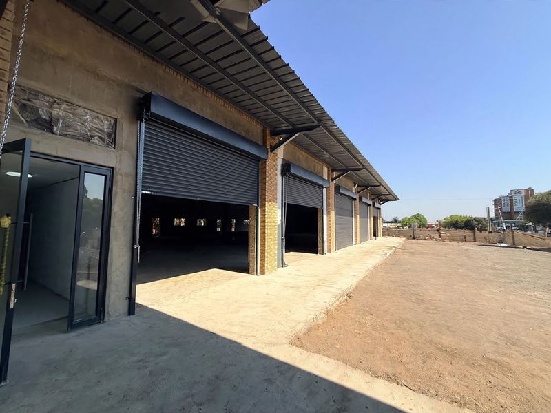 Front elevation of a retail warehouse property featuring multiple roller shutter doors, a concrete apron, and a metal roof structure.