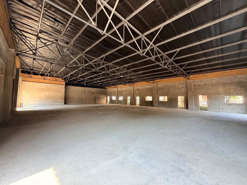 Spacious open-plan retail or industrial shell featuring exposed steel roof trusses, concrete flooring, and unplastered brick walls, offering a blank canvas for customization.