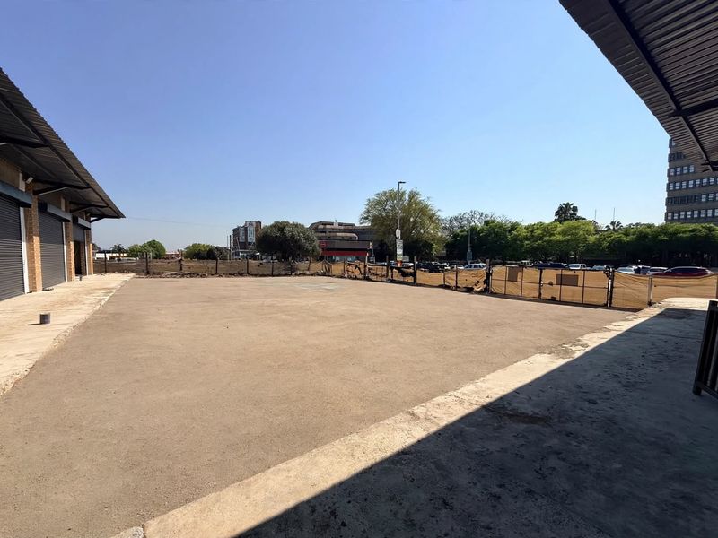 An expansive outdoor paved yard area featuring metal roof overhangs, roller shutter access, and perimeter fencing, suitable for commercial storage or parking.