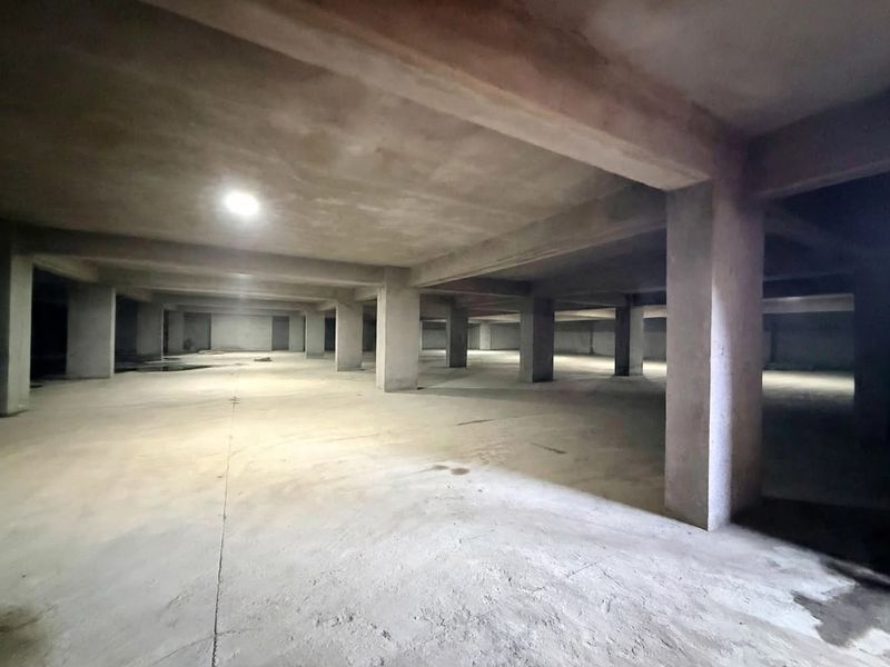 A large, open-plan unfinished concrete basement or garage space featuring structural columns and basic recessed lighting.