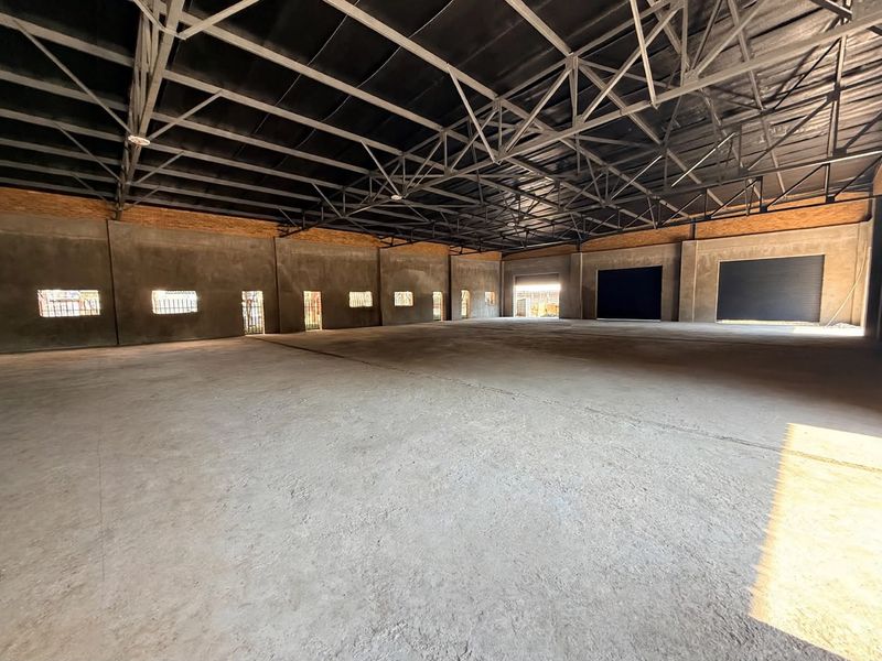 A large, open-plan industrial utility space featuring exposed steel roof trusses, concrete flooring, and multiple roller shutter access points.