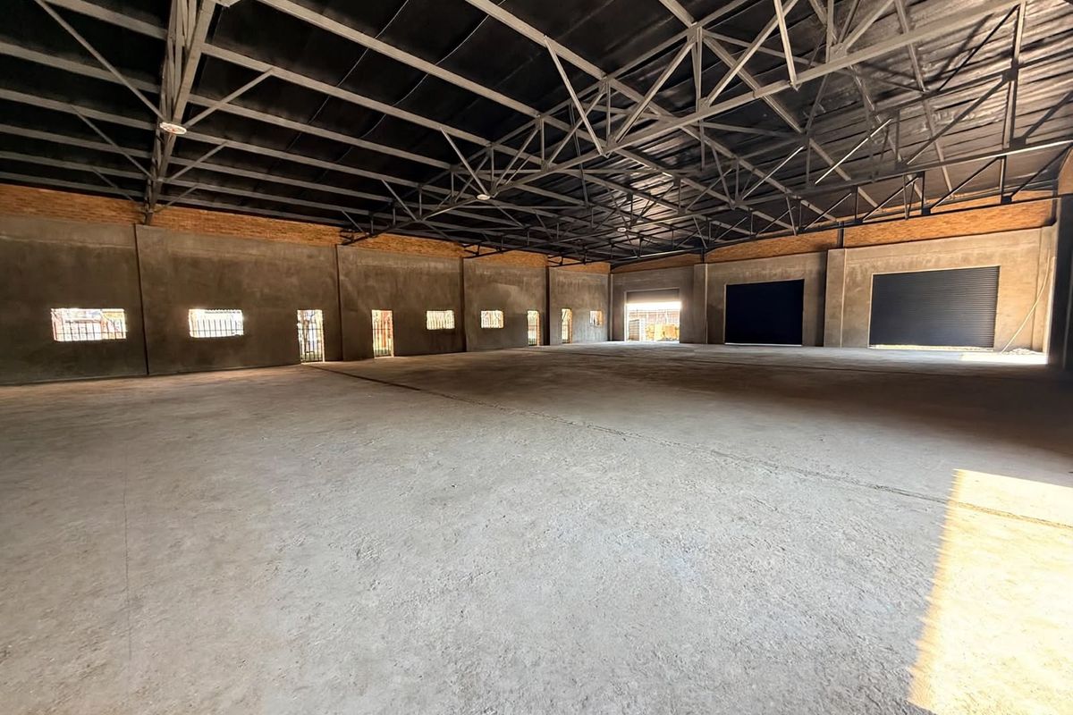 A large, open-plan industrial utility space featuring exposed steel roof trusses, concrete flooring, and multiple roller shutter access points.