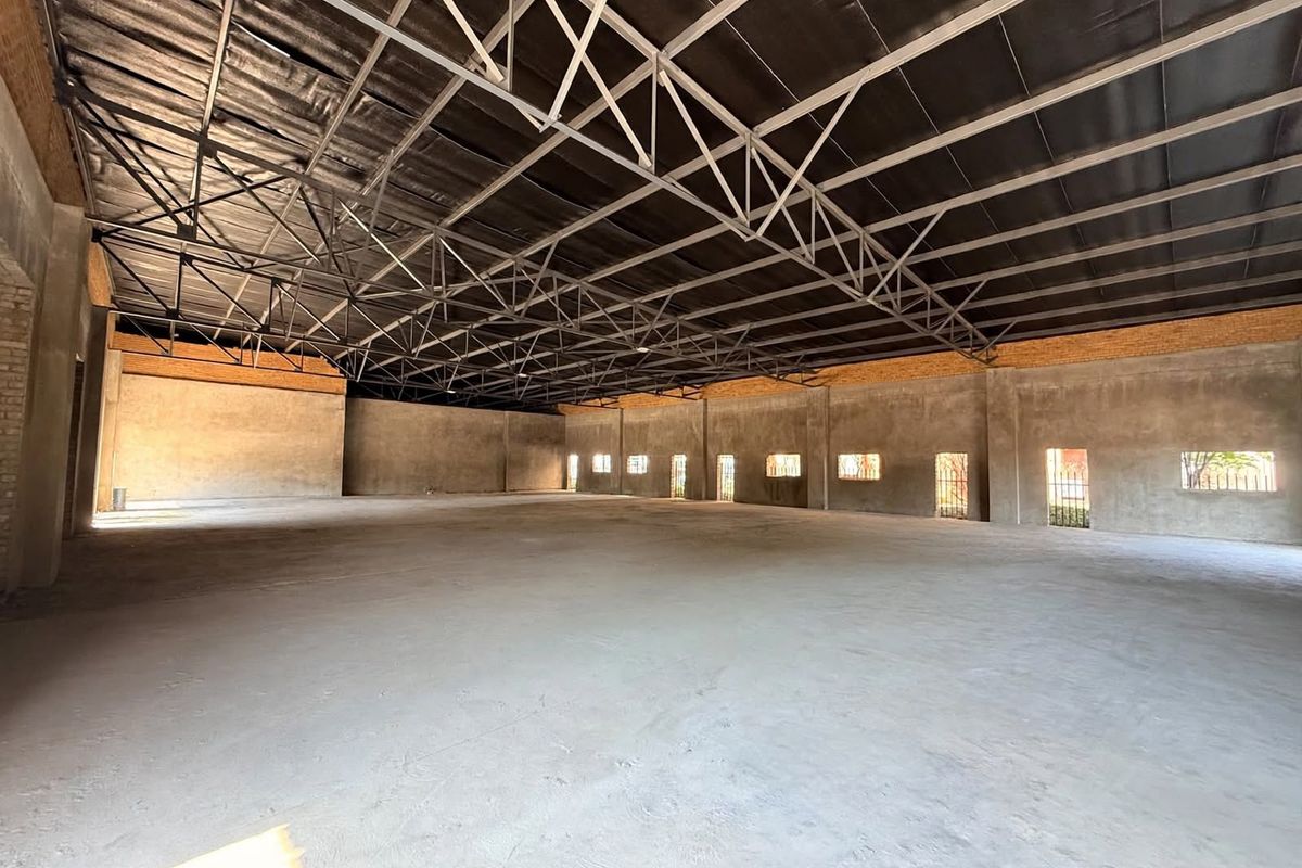 Spacious open-plan retail or industrial shell featuring exposed steel roof trusses, concrete flooring, and unplastered brick walls, offering a blank canvas for customization.