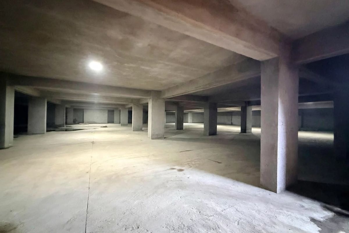 A large, open-plan unfinished concrete basement or garage space featuring structural columns and basic recessed lighting.