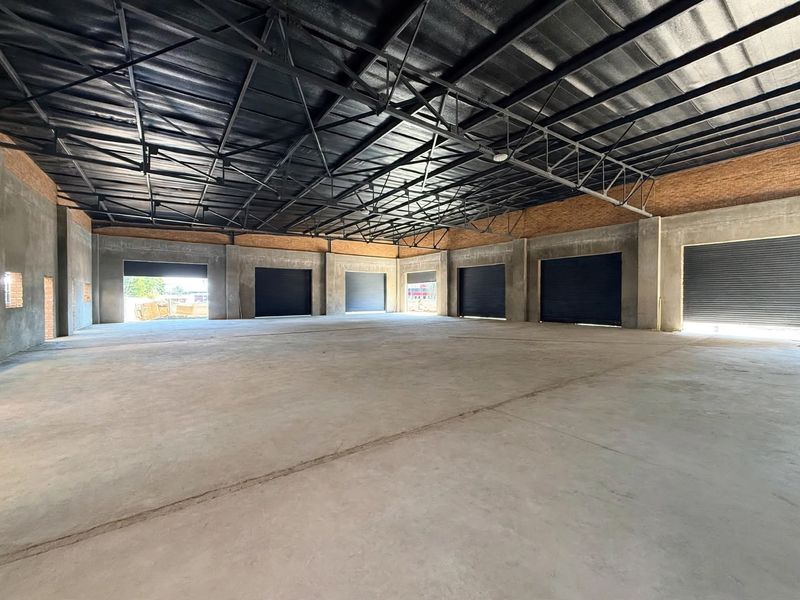 Spacious industrial warehouse unit featuring high exposed steel roof trusses, polished concrete flooring, and multiple roller shutter doors for easy access.