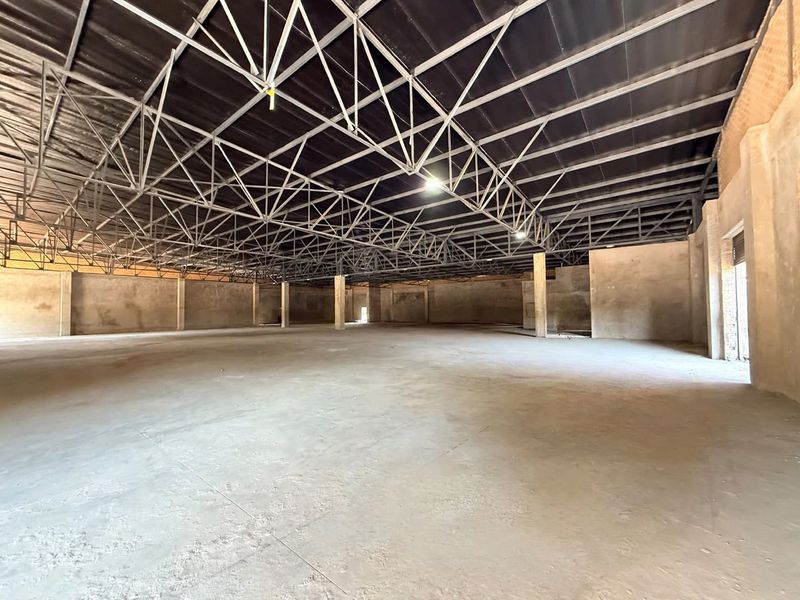 Expansive open-plan retail or industrial space featuring exposed steel roof trusses, concrete flooring, and structural support columns in a shell condition.