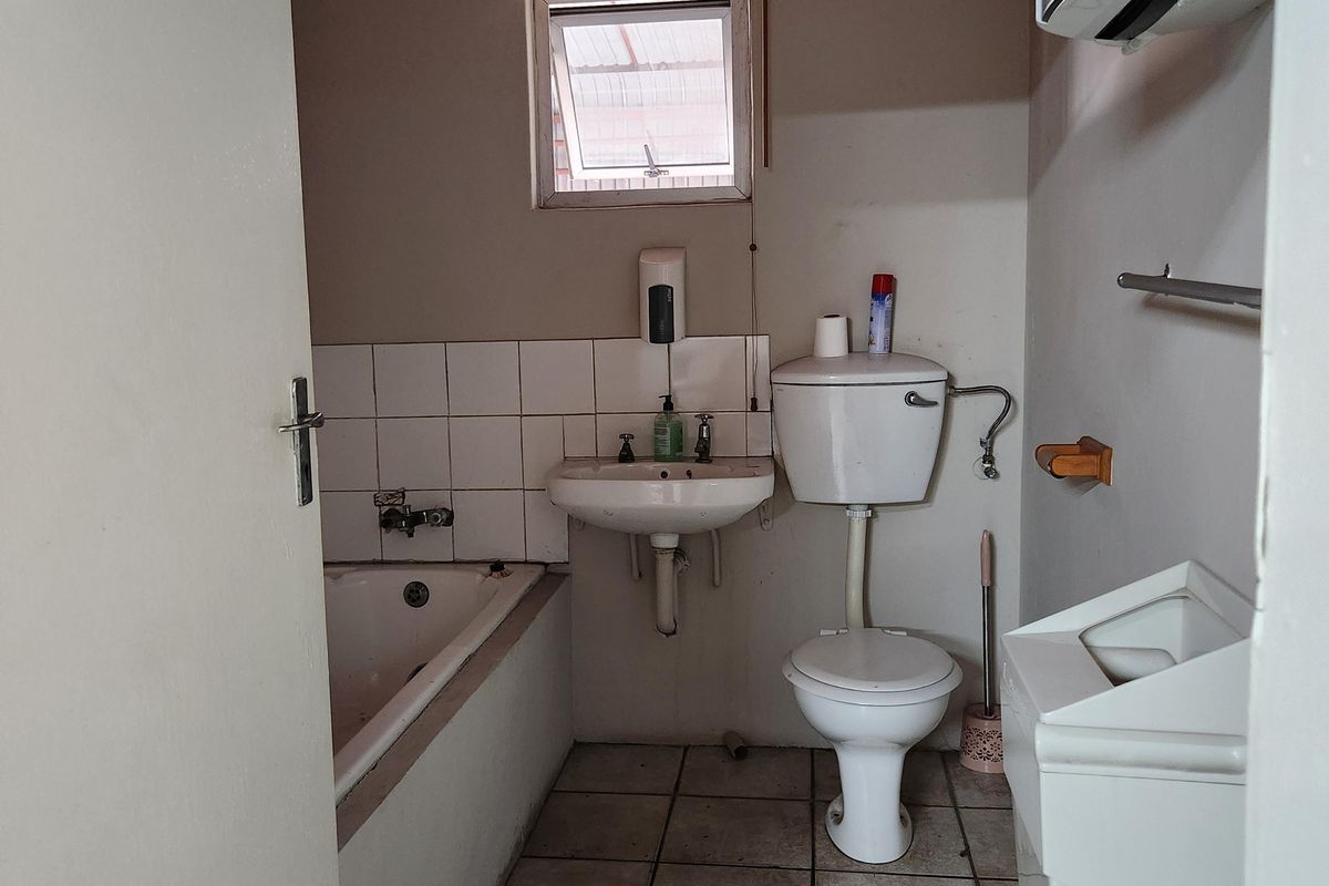 A functional industrial-style bathroom featuring a bathtub, wall-mounted basin, and toilet, with tiled flooring and basic wall finishes.