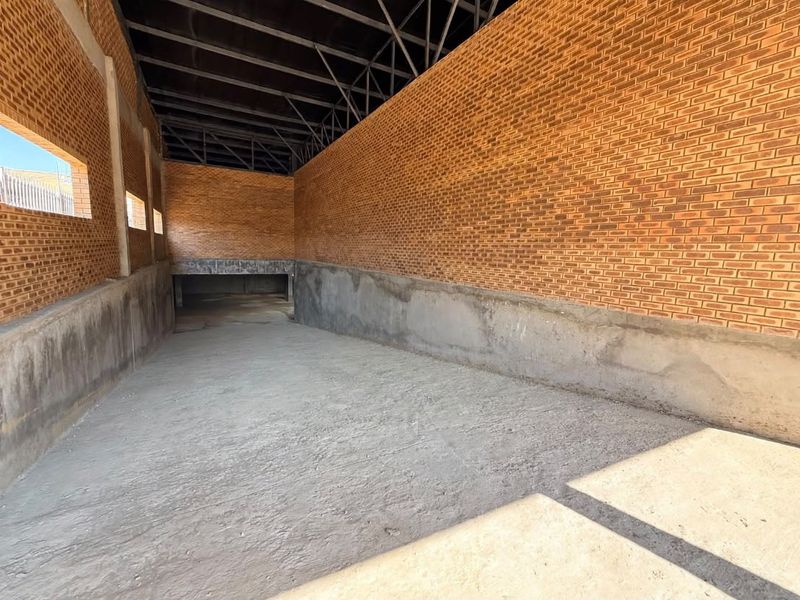 An unfinished utility or storage space featuring exposed brick walls, concrete flooring, and steel roof trusses with ramp access.