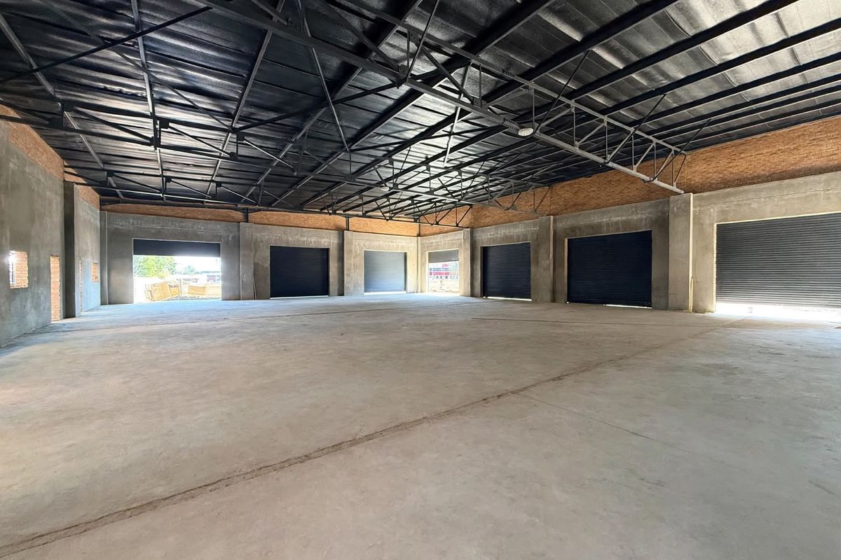Spacious industrial warehouse unit featuring high exposed steel roof trusses, polished concrete flooring, and multiple roller shutter doors for easy access.