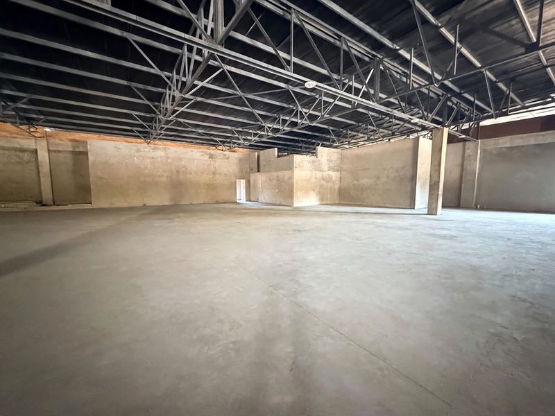 A large, open-plan retail space featuring exposed steel roof trusses, concrete flooring, and unfinished masonry walls, offering a blank canvas for custom fit-out.