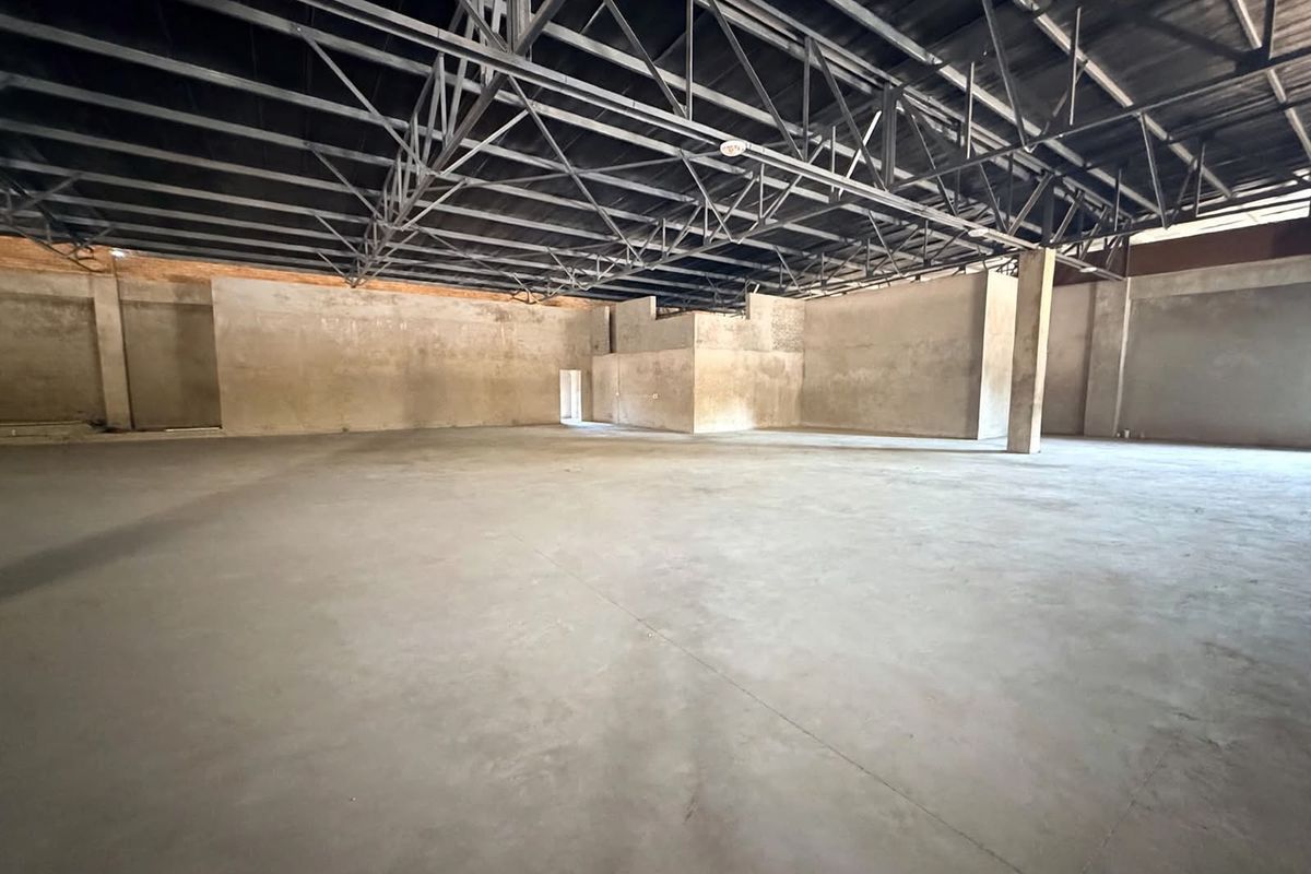 A large, open-plan retail space featuring exposed steel roof trusses, concrete flooring, and unfinished masonry walls, offering a blank canvas for custom fit-out.