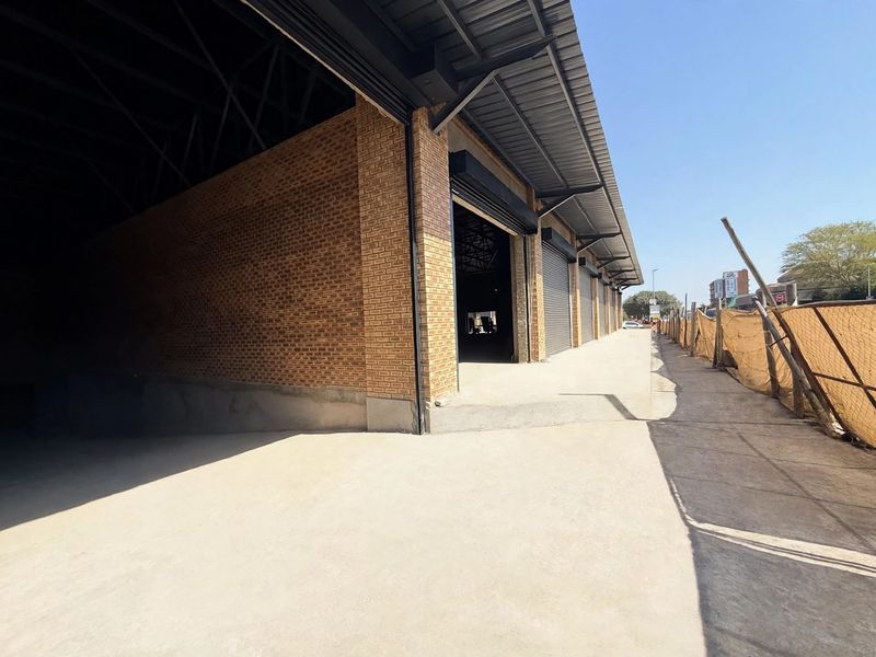 Exterior view of a modern industrial retail unit featuring exposed brickwork, concrete flooring, and multiple metal roller shutter doors under a steel roof structure.