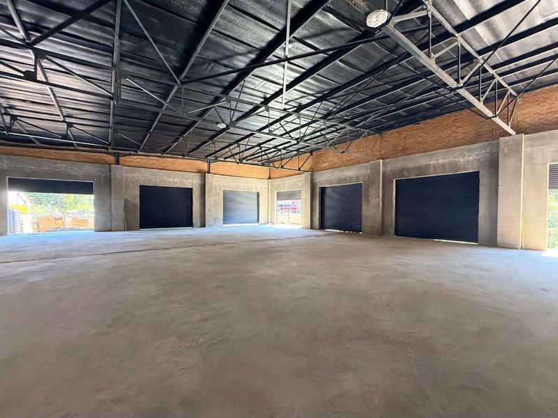 Spacious industrial warehouse unit featuring exposed steel roof trusses, polished concrete flooring, and multiple roller shutter doors for easy access.