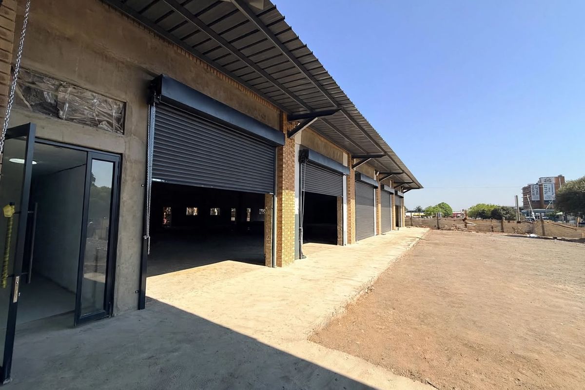 Front elevation of a retail warehouse property featuring multiple roller shutter doors, a concrete apron, and a metal roof structure.