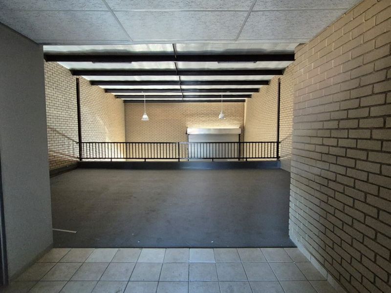 Spacious industrial utility area featuring exposed steel beams, brick walls, and a secure metal roller shutter door, suitable for storage or workshop use.