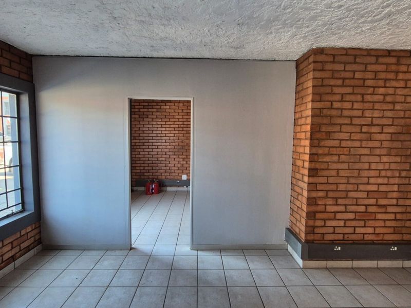 An empty industrial office space featuring exposed brick walls, tiled flooring, and a large window providing natural light.