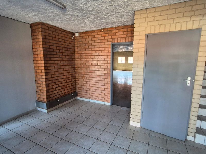 An empty industrial utility space featuring exposed brick walls, ceramic tiled flooring, and an internal staircase leading to an upper level.