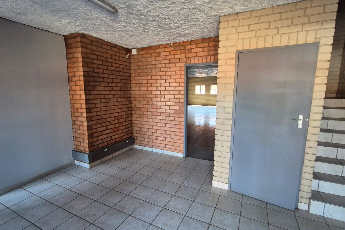 An empty industrial utility space featuring exposed brick walls, ceramic tiled flooring, and an internal staircase leading to an upper level.