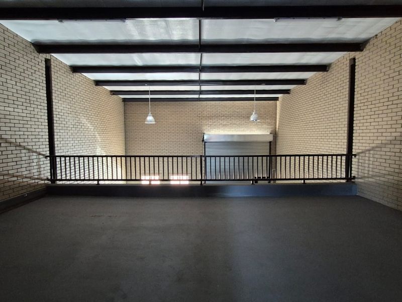 Spacious industrial mezzanine area featuring exposed steel beams, brick walls, and a secure metal railing overlooking the lower level.