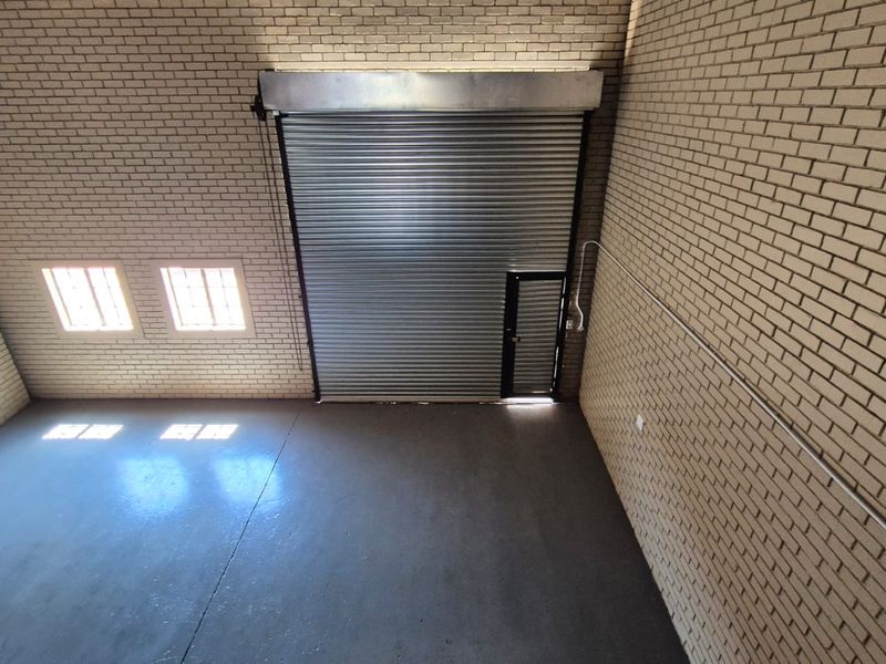 Spacious industrial utility area featuring high-clearance roller shutter door, durable concrete flooring, and exposed brick walls, suitable for storage or workshop use.