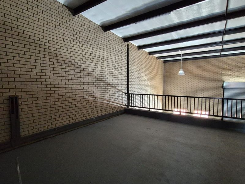 An open-plan industrial mezzanine level featuring exposed brick walls, steel structural beams, and a secure metal railing overlooking the lower floor.