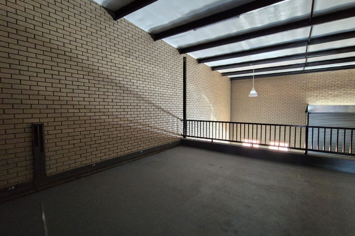 An open-plan industrial mezzanine level featuring exposed brick walls, steel structural beams, and a secure metal railing overlooking the lower floor.