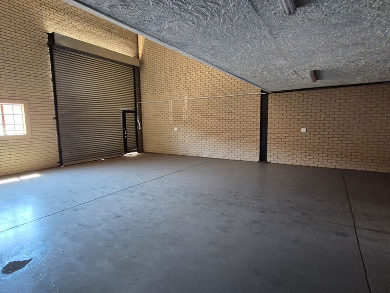 Spacious industrial garage featuring high ceilings, exposed brick walls, concrete flooring, and a large roller shutter door for vehicle or equipment access.