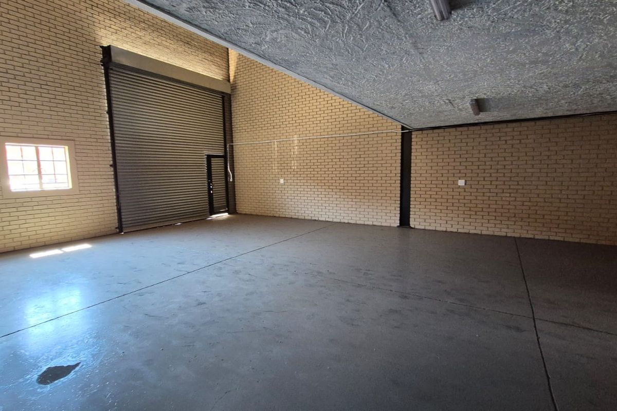 Spacious industrial garage featuring high ceilings, exposed brick walls, concrete flooring, and a large roller shutter door for vehicle or equipment access.